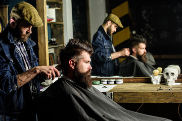 Barber with hair clipper works on hairstyle for man with beard, barbershop background. Barber...