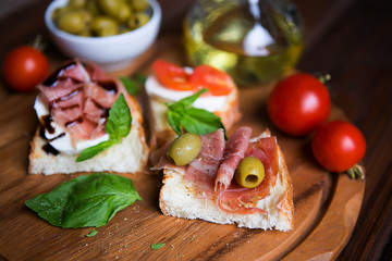 Appetizing bruschettes with jamon, tomatoes, basil, mozzarella, olives and oil on a dark wooden board