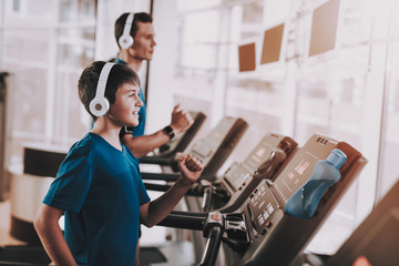 Fototapeta na wymiar Young Father and Son Training on Treadmills in Gym