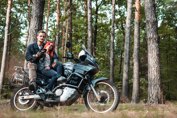 Fototapeta na wymiar Outdoor shot of happy young romantic couple with big motorcycle for tourism and travel. autumn forest background, traveling together, off road, red hair girl