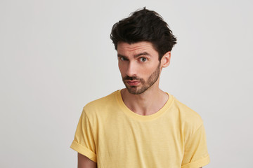 Fototapeta premium Closeup of serious handsome young man with bristle wears yellow t shirt feels confident and looks directly in camera isolated over white background