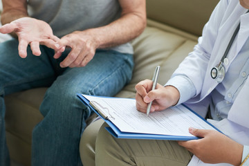 Crop shot of doctor during home visit to senior man listening to complaints and writing them down...