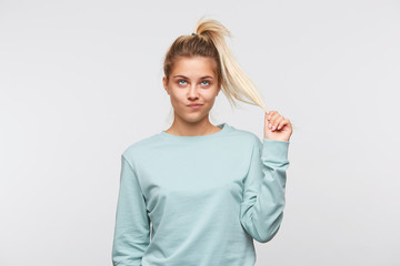 Closeup of unhappy pretty young woman with blonde hair and ponytail wears blue sweatshirt feels displeased and looks up isolated over white background