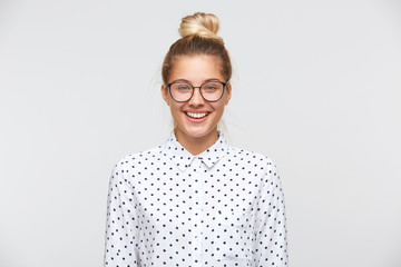 Closeup of smiling pretty young woman with bun wears polka dot shirt and glasses feels happy and...