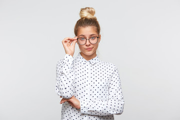 Portrait of unhappy sad young woman with bun wears polka dot shirt and spectacles feels...