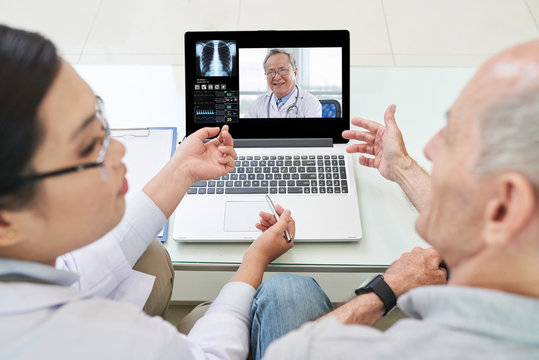 Back View Of Communicating Senior Man And Doctor Sitting On Sofa And Watching Laptop Having Discussion