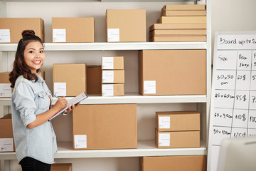 Portrait of female office worker standing near the shelves with online shopping box parcel in...