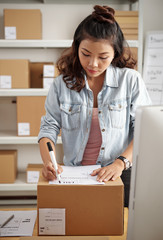 Asian young woman filling the form on cardboard box at her workplace