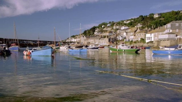 Camera rises from breaking waves over harbour of Mousehole in Cornwall