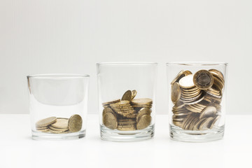 Monedas dentro de hucha de vasos de cristal sobre fondo blanco y gris aislado. Vista de frente. Concepto ahorro. Copy space - obrazy, fototapety, plakaty