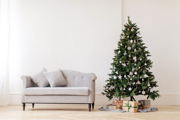 Beautiful decorated Christmas tree with gifts placed under standing near gray couch on background...