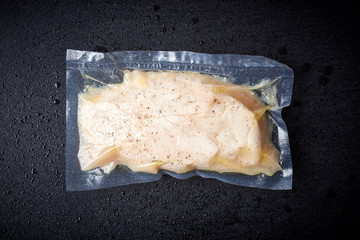 Chicken breast vacuum sealed on black table, from above