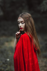 mystic girl in red cloak and elegant wreath in forest