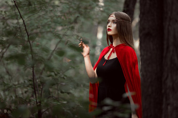 mystic young woman in red cloak in forest