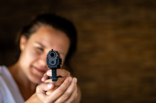 Young woman holding a gun and aiming toward a camera. Pistol in hand and pointing.