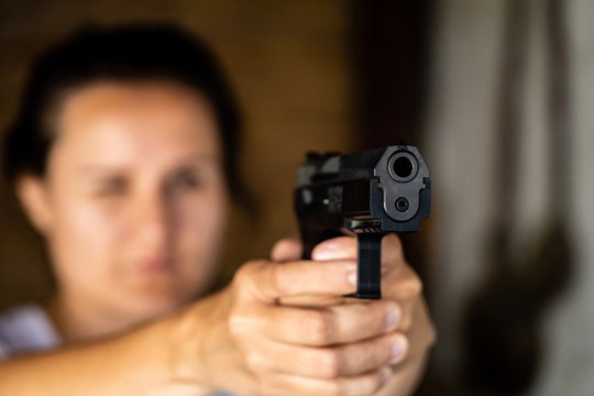 Young woman holding a gun and aiming. Pistol in hand and pointing.