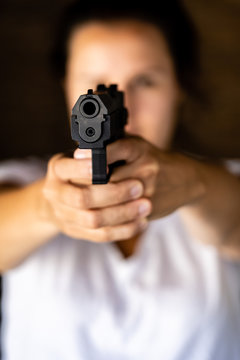 Young woman holding a gun and aiming toward a camera. Pistol in hand and pointing.