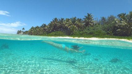 HALF UNDERWATER: Young woman on holiday diving in the crystal clear ocean water.