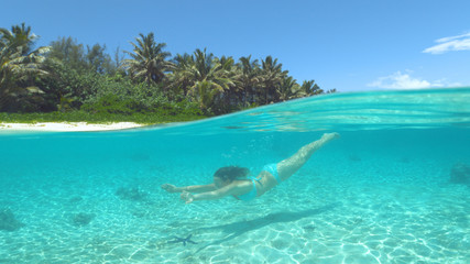 HALF UNDERWATER: Cheerful girl swimming underwater in the crystal clear ocean.