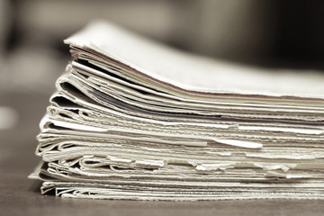 Thick pile of newspapers and magazines on wooden table, side view, selective focus on paper with blurred background