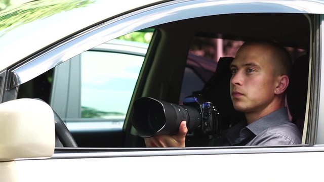 Young Male Spy Sits In The Car Taking Photos To The Camera With A Zoom Lens. Detective Agency Concept