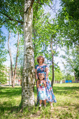 Obraz na płótnie Canvas grandmother and granddaughter embrace and play, stand in the forest near the birch