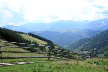Fototapeta na wymiar Beautiful landscape with view to wooden fence, pasture, forest and mountains.