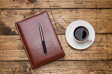 Diary in leather cover and Cup of coffee on wooden background. Education and office concept.