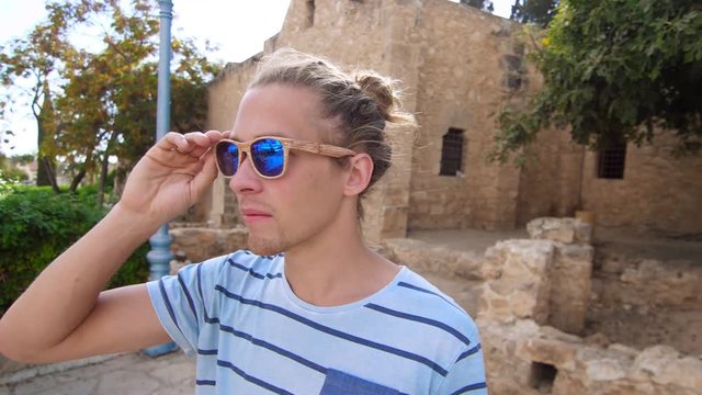 Hipster man wearing sunglasses. Close up of male face in sunglasses looking away. Male tourist in sun glasses enjoy Cyprus city travel. Traveler in tropical city