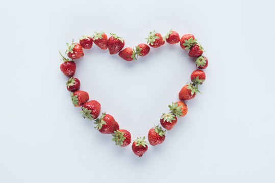 top view of heart shape sign made of fresh strawberries on white surface