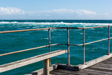 Fototapeta na wymiar A bench seat on the Port Noarlunga Jetty looking out to the rough seas and reef in South Australia on 6th September 2018