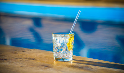 Glass of mineral water with lemon and ice near waterpool on the wood texture