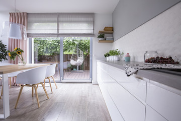 Hanging chair on a wooden patio of a modern house with white kitchen interior. Real photo of...