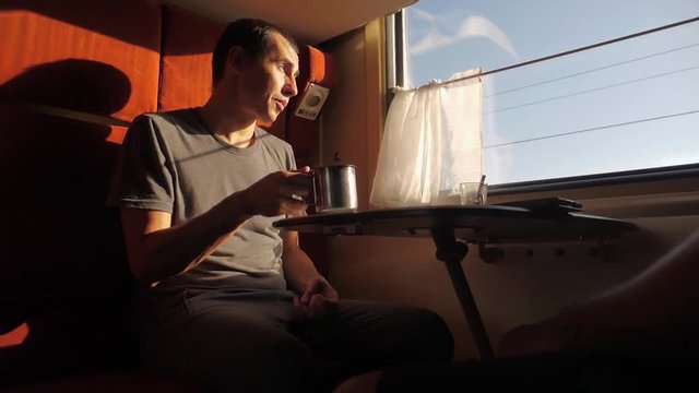 man is sitting in a Railway carriage train at the window of a compartment the car is drinking tea and coffee is talking. slow motion video. two men drinking tea on the train talking the train social