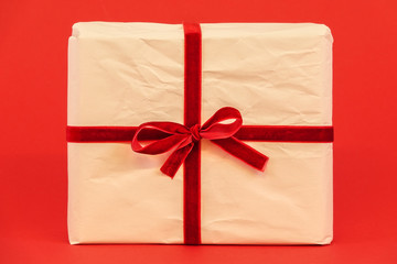 Christmas gift box on red background. White recycled / reused wrapping paper with red ribbon.