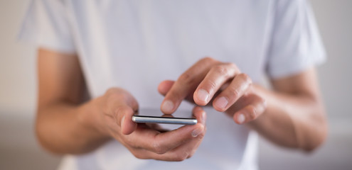 Panoramic of young caucasian man using apps on a touchscreen smartphone - Hands close-up focus on phone - Concept for using technology, shopping online, using mobile apps, texting, phone addiction