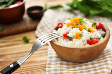 Bowl with tasty boiled rice and vegetables on wooden table