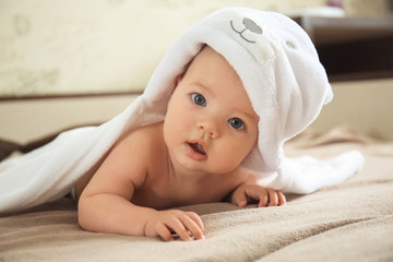 Cute baby with towel lying on bed at home