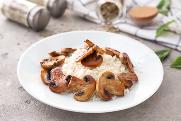 Plate with tasty boiled rice and mushrooms on light table