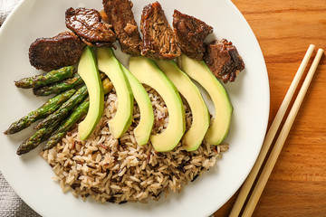 Plate with boiled rice, vegetables and meat on wooden table