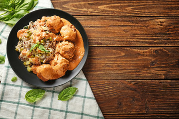 Plate with boiled rice, vegetables and meatballs on wooden table