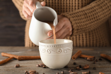 Woman pouring tasty cocoa from jug into cup on wooden table