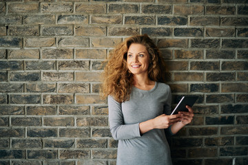 Portrait of woman using tablet in front of brick wall.