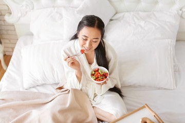 Asian woman eating healthy fruit salad for breakfast at home
