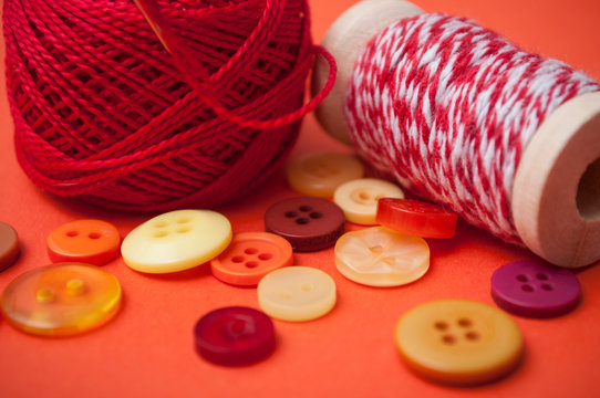 closeup of buttons and bobbins of cotton yarn on orange background