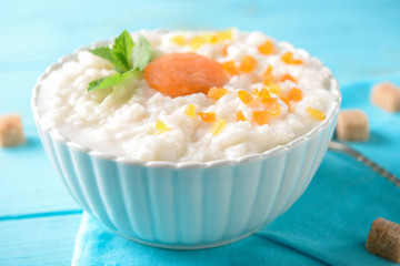 Bowl with delicious rice pudding and dry apricots on color table