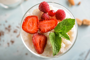 Glass with delicious rice pudding and berries on light background, top view