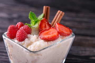 Glass bowl with delicious rice pudding and berries on table, closeup