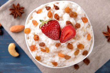 Bowl with delicious rice pudding, raisins and strawberry on napkin