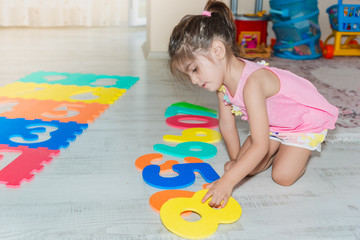 Little girl sits and holds colorful puzzle play mat